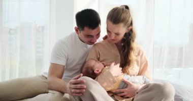 Happy parents looking at baby son sleeping in arms while sitting on bed