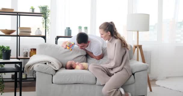Father with mother playing and kissing baby son lying on sofa — Stockvideo
