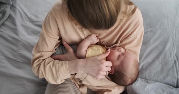 Young mother watching her baby son sleeping in arms on bed — Stockvideo