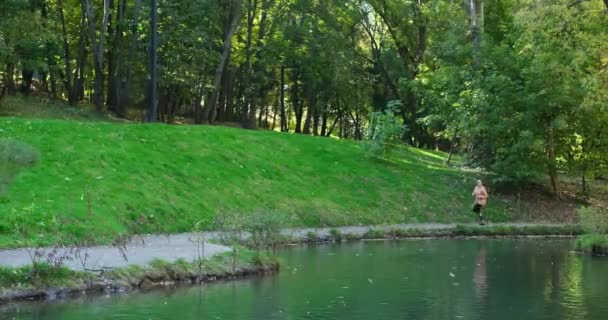 Young woman running by lake in forest — Stock Video