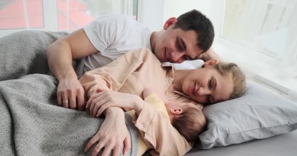 Parents with baby son sleeping in arms while lying on bed — Stockvideo