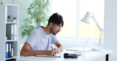 İşadamı ofiste not yazıyor ve laptop kullanıyor.