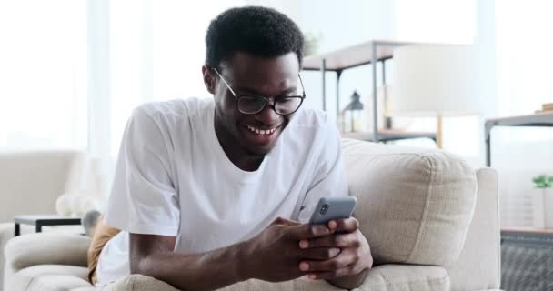 Молодий чоловік лежить на дивані і використовує мобільний телефон — стокове відео
