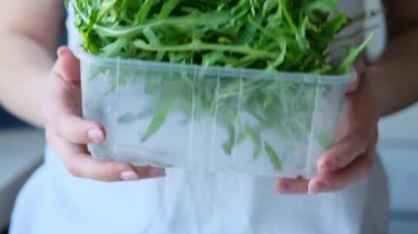 Woman tossing fresh arugula leaves in container