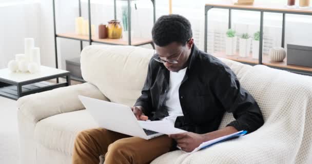 Бізнесмен працює з ноутбуком і аналізує документи на дивані — стокове відео