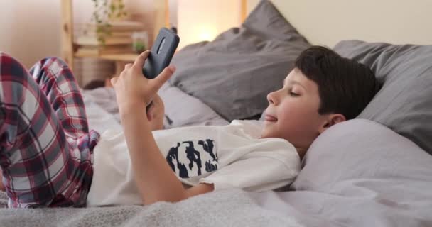 집에서 침대에서 휴대 전화를 사용하는 소년 — 비디오