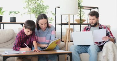 Anne ve oğul ev ödevi yaparken baba evde çalışıyor.