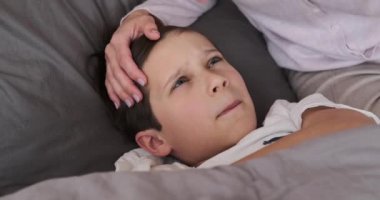 Mother checking temperature of unwell son in bedroom