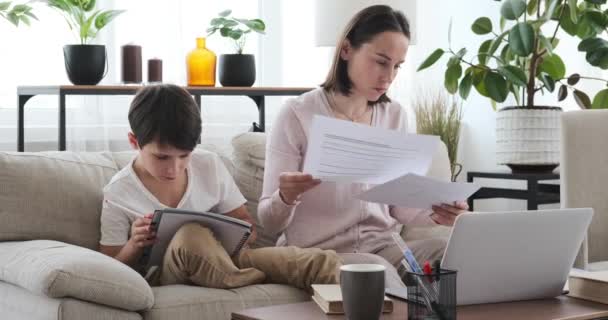 Madre ayudando a su hijo con la tarea mientras trabaja en el ordenador portátil en casa — Vídeos de Stock