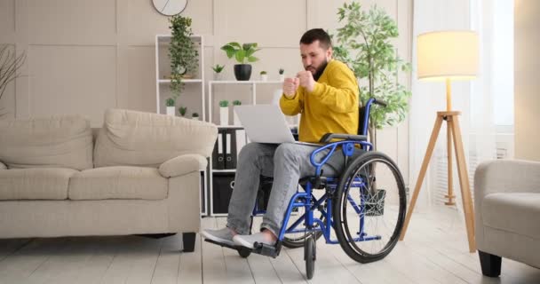 Funksjonshemmet mann som danser og beveger seg rundt på rullestol ved bruk av bærbar datamaskin – stockvideo