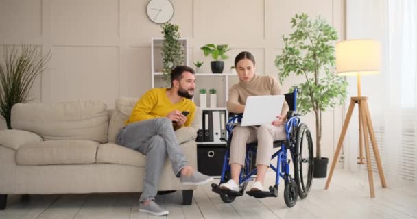 Mujer discapacitada discutiendo trabajo con el marido mientras trabaja en el ordenador portátil — Vídeo de stock