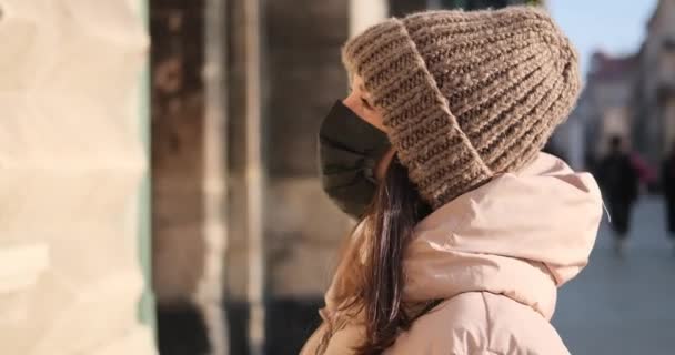 Mujer en chaqueta con capucha y sombrero de punto con máscara protectora al aire libre — Vídeos de Stock