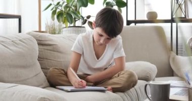 Evdeki kanepede kitap yazan çocuk.