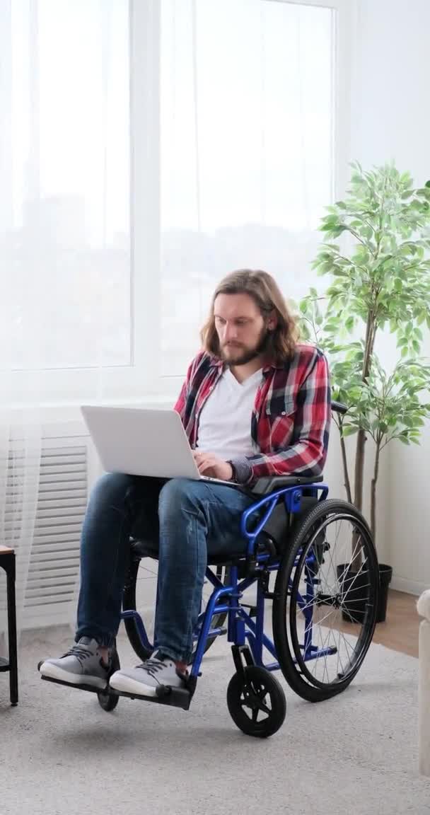 Hombre de diferentes capacidades sentado en silla de ruedas y trabajando en el ordenador portátil — Vídeo de stock