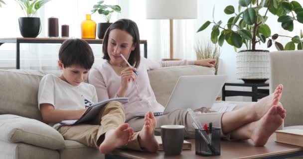 Mãe ajudando filho com lição de casa enquanto trabalhava no laptop em casa — Vídeo de Stock