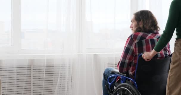 女人推着丈夫坐轮椅从窗户往外看 — 图库视频影像