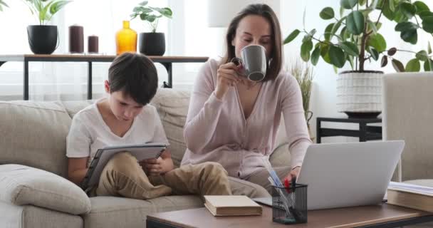 家でノートパソコンで仕事をしながら息子を助ける母親 — ストック動画
