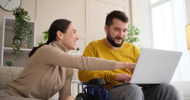 Ζευγάρι απολαμβάνει τη χρήση φορητού υπολογιστή με τον άνθρωπο σε αναπηρική καρέκλα — Αρχείο Βίντεο