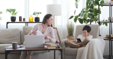 Oğlu cep telefonu kullanırken annesi evde çalışmakla meşgul.