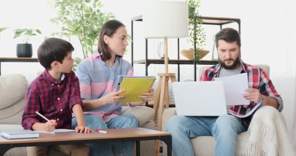 Pais ajudando filho com lição de casa, enquanto o pai está trabalhando no laptop em casa — Vídeo de Stock