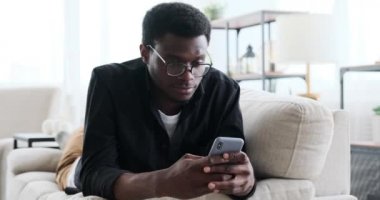 Adam kanepede uzanıyor ve cep telefonu kullanıyor.