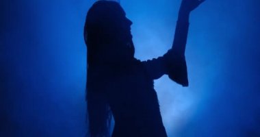 Mavi ışıkta ve dumanda dans eden kadın silueti