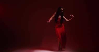 Uzun saçlı kadın kırmızı ışıkta dans ediyor ve sigara içiyor.