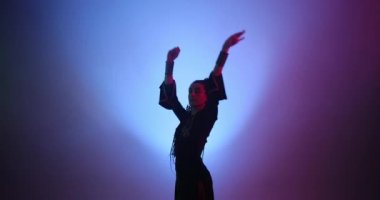 Uzun saçlı güzel bir kadın mor ışıkta ve dumanda dans ediyor.