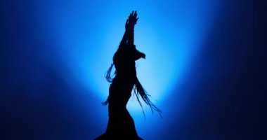 Mavi ışık ve dumanla dans eden uzun saçlı bir kadının silueti.