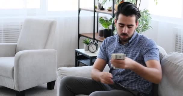 Młody człowiek liczy pieniądze siedząc na kanapie — Wideo stockowe