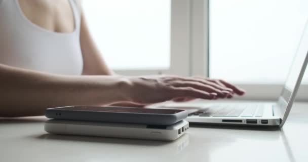 Kobieta pracująca na laptopie z telefonem komórkowym i powerbank na biurku — Wideo stockowe