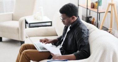 Kanepede dizüstü bilgisayar kullanarak çalışan Afro-Amerikalı iş adamı.