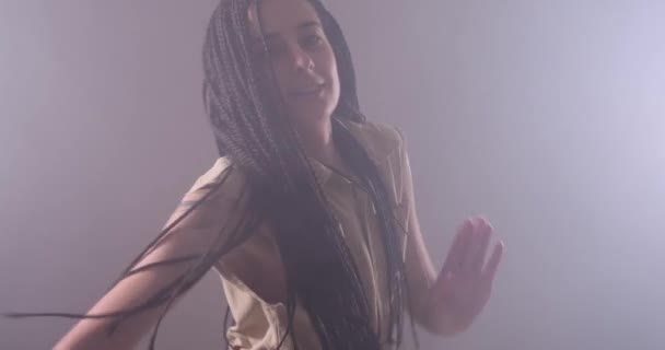 Женщина с длинными волосами танцует на освещенном фоне и курит — стоковое видео