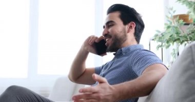 Kanepede oturan ve cep telefonuyla konuşan adam.