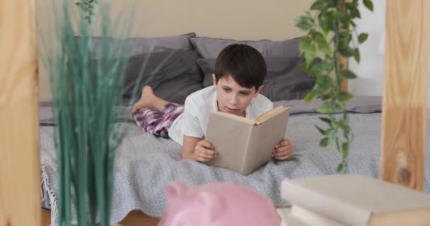 Pojke läser en bok i sängen — Stockvideo