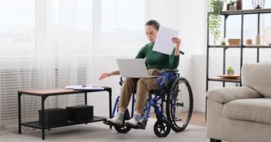 Tekerlekli sandalyedeki engelli kadın laptop kullanıyor ve belgeleri analiz ediyor.