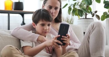 Anne ve oğlu evdeki koltukta cep telefonu kullanıyor.