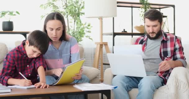 Madre con hijo haciendo la tarea mientras el padre está trabajando desde casa — Vídeos de Stock