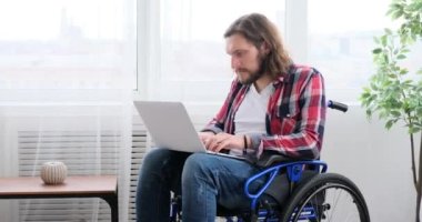 Tekerlekli sandalyedeki engelli adam dizüstü bilgisayar kullanıyor.