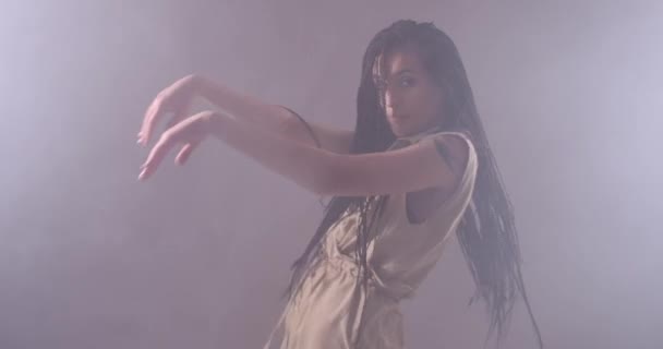 Женщина с длинными волосами танцует на освещенном фоне и курит — стоковое видео