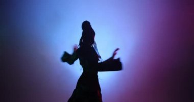 Uzun saçlı güzel bir kadın mor ışıkta ve dumanda dans ediyor.