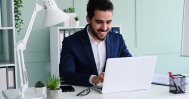 Genç işadamı dizüstü bilgisayarda yazıyor ve gülümsüyor.