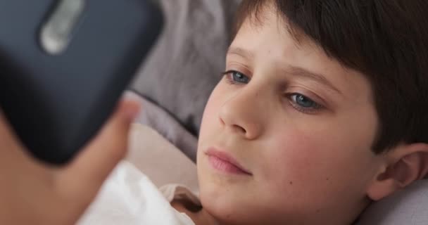 Mobiltelefont használó fiú otthon az ágyban — Stock videók