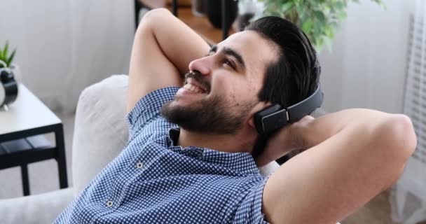 Hombre escuchando música en los auriculares mientras se apoya en el sofá — Vídeo de stock