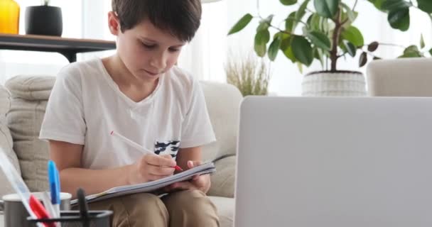 Menino usando laptop e escrevendo em livro em casa — Vídeo de Stock