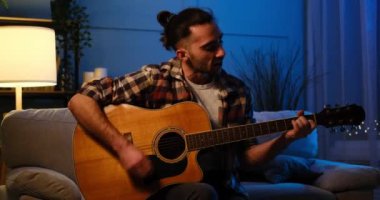 Evde gitar çalan ve şarkı söyleyen bir adam