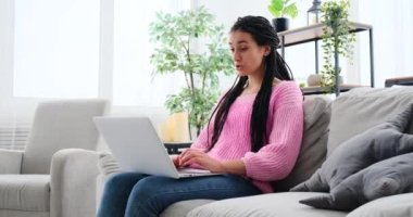 Kanepeye oturmuş dizüstü bilgisayar kullanan bir kadın görüntüsü.