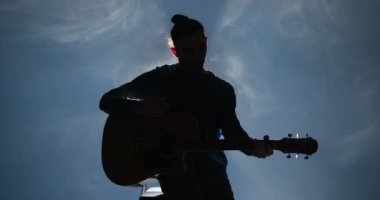 Gitar çalan genç adamın silueti.