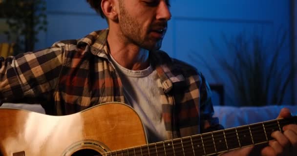 Young man singing and playing guitar sitting on sofa — Stock Video