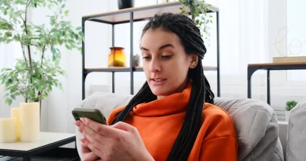 Mulher feliz relaxando no sofá enquanto conversa usando o telefone móvel — Vídeo de Stock